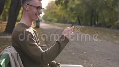 年轻的<strong>街头风</strong>格的男人喜欢在公园里使用他的智能手机，年轻的白种人戴着眼镜